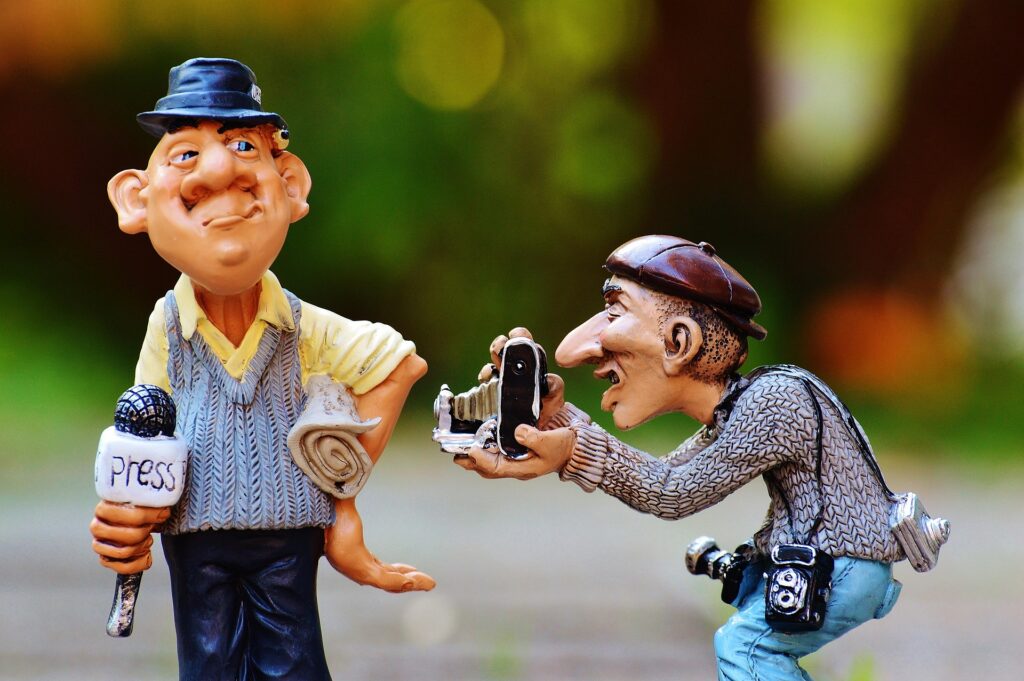 Due statuine in ceramica che rappresentano un giornalista con microfono "PRESS" in mano e un fotografo con macchina fotografica, che simboleggiano l'importanza di educare per i media.